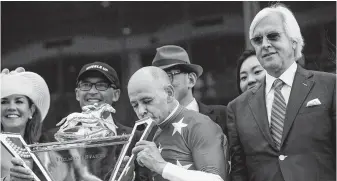  ?? Victor J. Blue / New York Times ?? Mike Smith, the jockey who won the Belmont Stakes aboard Justify, kisses the Triple Crown trophy while celebratin­g with trainer Bob Baffert, right, at Belmont Park on Saturday.