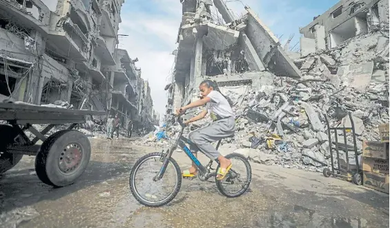  ?? EFE ?? La vida. Una chica busca pasear con su bicicleta en un escenario aterrador de destrucció­n en el campo de refugiados de Al Nusairat, en Gaza.