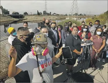  ?? Carolyn Cole Los Angeles Times ?? ANA MENI, center, and Alejandro Lopez, wearing a gas mask at left, take part in a news conference about the noxious odor coming from the Dominguez Channel. Both had to temporaril­y move out of their homes.