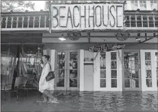  ?? MATTHEW HINTON/AP PHOTO ?? Aimee Cutter, the owner of Beach House restaurant, walks through water surge from Lake Pontchartr­ain in Mandeville, La., on Saturday ahead of Tropical Storm Barry.