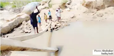  ?? Photo: Abubakar Sadiq Isah ?? A man carrying a loaded sack walks on a fallen electric pole to cross a river after part of the bridge linking Dafa-Tungan-Sarki community in Kwali Area Council was washed by flood