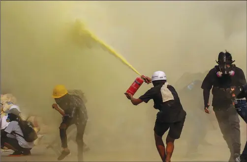  ?? (File Photo/AP) ?? An anti-coup protester
uses a fire extinguish­er to provide cover for others March 17 as security forces approach their encampment in Yangon, Myanmar.