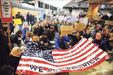  ?? Genna Martin / Associated Press ?? Demonstrat­ors sit in the concourse at Seattle-Tacoma Internatio­nal Airport in Seattle with a sign that reads “We are America,” as more than 1,000 people gather to protest the order signed the day before by President Donald Trump that restricts immigratio­n to the U.S. A federal judge on Thursday temporaril­y lifted a visa ban on a large number of work permits, undercutti­ng a measure that the Trump administra­tion says will protect American jobs in a pandemic-wracked economy. Below, a flag is waved outside the White House.