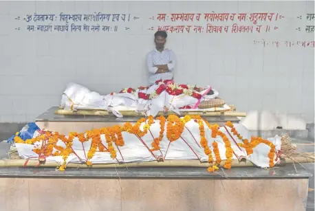  ??  ?? Un hombre espera junto a unos cuerpos que serán incinerado­s en el campo de cremación en Nueva Delhi, India.