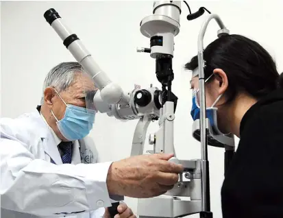  ??  ?? Zhang checks the eyes of a patient. He sees patients every Tuesday as long as his health permits.