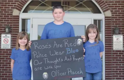  ?? BRIANA CONTRERAS — THE MORNING JOURNAL ?? From left, Sheffield Lake youngsters Natalie Brown, 7, Timothy Rowe, 11, and Trista Rowe, 7, wear blue and hold a sign made for Amherst police officer Eugene Ptacek who was wounded during a shoot out May 31.