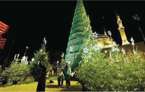  ?? Reuters ?? A Muslim woman takes a selfie with her family yesterday in front of a Christmas tree designed by Lebanese designer Elie Saab, located in front of Al Ameen Mosque in Beirut, Lebanon.