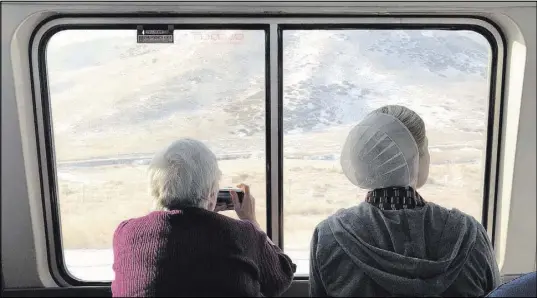  ??  ?? Two women take photos of the Sierra Nevada mountains while riding on Amtrak’s California Zephyr.