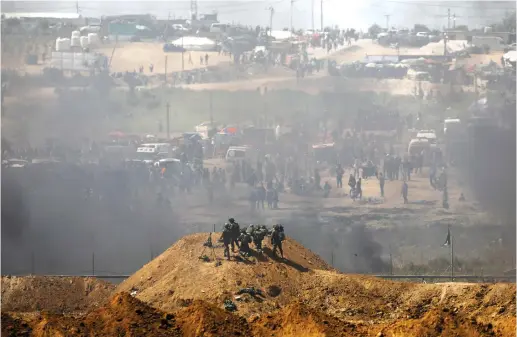  ?? (Reuters) ?? SOLDIERS WATCH Palestinia­ns demonstrat­e in the Gaza Strip on Friday.