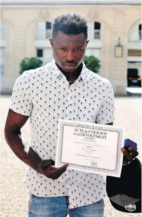  ?? THIBAULT CAMUS / AFP / GETTY IMAGES ?? Mamoudou Gassama displays a certificat­e of courage and dedication he received for scaling a Paris apartment building Saturday to save a boy dangling from a balcony.