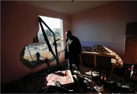  ?? Reuters ?? A Palestinia­n looks out of his apartment after it was damaged in an Israeli air strike in the northern Gaza Strip yesterday