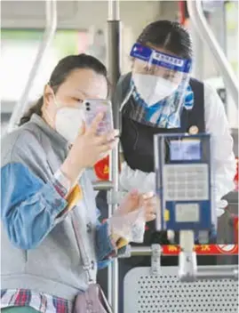  ?? ?? A passenger shows her health code and PCR test result to the conductor on a public transport bus in Shanghai yesterday. — Xinhua