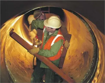  ?? Al Schaben Los Angeles Times ?? METROPOLIT­AN Water District workers fit a section of new custom-made steel pipe to replace the original concrete pipeline in Irvine after it ruptured in December 1999. The blowout spilled 5 million gallons of water.