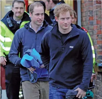  ??  ?? Les princes William et Harry, en bottes de caoutchouc, ont donné un coup de main aux militaires en transporta­nt des sacs de sable à Datchet, en Angleterre.