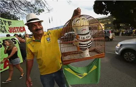  ?? — AP ?? Lula the jailbird: A demonstrat­or holding a bird cage featuring a small doll of Lula dressed as a prisoner in Brasilia.