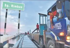  ??  ?? Workers unload high-density polyethyle­ne (HDPE) pipes meant to be laid along the temporary line across Tandang Sari bridge as a way to supply water to the villagers at Kampung Pusa Seberang.