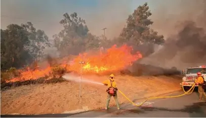 ?? MIKE ELIASON/SANTA BARBARA COUNTY FIRE DEPARTMENT VIA AP ?? Firefighte­rs extinguish a roadside wildfire in Goleta, California, earlier this month.