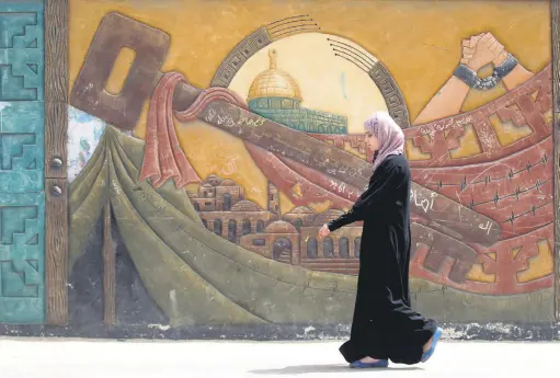  ??  ?? A Palestinia­n woman walks past a mural in the Khan Yunis refugee camp, southern Gaza Strip, May 15, 2016, on the anniversar­y of the Nakba.