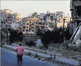  ?? Sergei Grits ?? The Associated Press A man rides his bicycle near damage in the old town of Homs, Syria, on Wednesday. The Russian Defense Ministry said it is coordinati­ng efforts to help Syrian refugees return home and rebuild the country’s infrastruc­ture destroyed by the civil war.