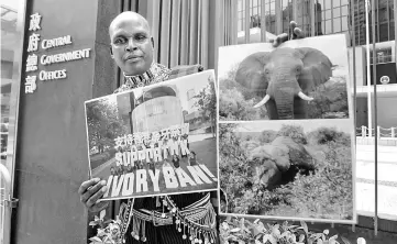  ??  ?? Park ranger Chris Leadismo, the head of wildlife security at NGO Save the Elephants in northern Kenya, holds up a photo (left) taken the day before showing acitivists holding letters which read ‘Support HK Ivory Ban!’ and photos of an elephant before (top) and after it was killed for its tusks, after a public hearing at the Legislativ­e Council (Legco) on a government proposal to ban the sale of ivory in Hong Kong. — AFP photo