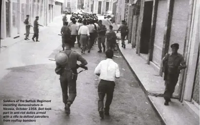  ??  ?? Soldiers of the Suffolk Regiment escorting demonstrat­ors in Nicosia, October 1958. Bell took part in anti-riot duties armed with a rifle to defend patrollers from rooftop bombers