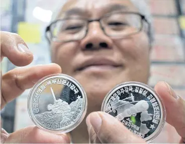  ?? AP ?? Coin dealer Joseph Poh displays two North Korean coins depicting its rockets programme in Singapore.
