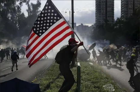  ?? Kin Cheung/ Associated Press ?? A protester runs with a U. S. flag as tear gas is released Monday in Hong Kong. Droves of protesters filled public parks and squares in several Hong Kong districts in a general strike staged on a weekday to draw more attention to their demands that the semi- autonomous Chinese city’s leader resign.