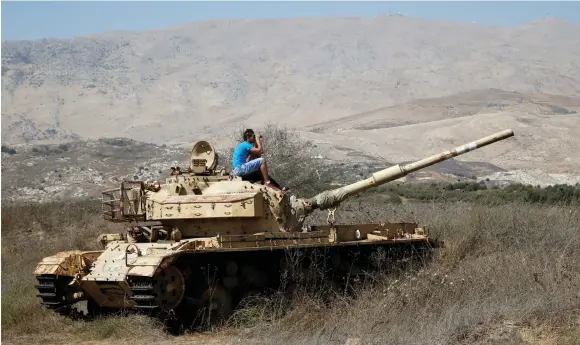  ?? (Reuters) ?? A MAN sits on an old tank as he watches fighting taking place in Syria from the Israeli side of the border fence.