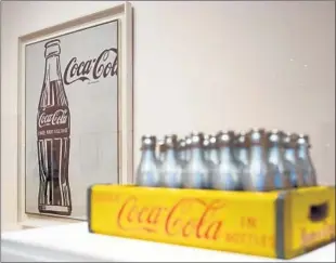  ?? Branden Camp Associated Press ?? THE HIGH MUSEUM in Atlanta has the exhibition “The Coca-Cola Bottle: An American Icon at 100,” which includes a piece by artist Andy Warhol, left, next to a case of Coca-Cola bottles. The museum organized the show in collaborat­ion with the Coca-Cola Co.