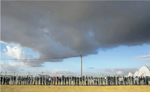  ?? ODED BALILTY/THE ASSOCIATED PRESS FILES ?? In this Feb. 17, 2014, file photo, African migrants stand inside Holot detention centre as others protest outside against the detention centre near Ktsiot in the Negev Desert in southern Israel.