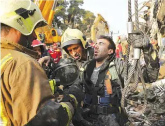  ??  ?? TEHRAN: Iranian firefighte­rs help their colleague yesterday during debris removal at the Plasco building which caught fire and collapsed on Thursday. — AP