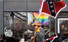  ?? ?? Paolo Bifulco (right) watches through the window from Heliotrope Brewery as confederat­e re-enactors and supporters march in Lexington, Virginia, during Lee-Jackson Day celebratio­ns.