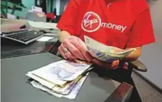  ?? Bloomberg ?? An employee counts pound notes at a Virgin Money’s branch. Virgin Money shares rose 2 per cent before paring gains on news of a merger with mid-sized bank CYBG.