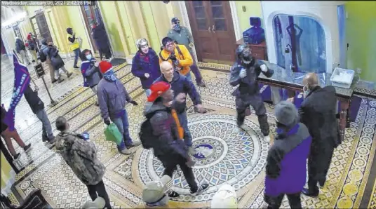  ?? FBI ?? In a clip from security surveillan­ce video, an individual who later was identified by the FBI as Ronald Sandlin entered wearing a bright orange sweatshirt and carrying what appeared to be camera equipment. “Person 1” can be seen putting up his fists as if to start boxing with one of retreating Capitol officers. As the officer stepped away, “Person 1” was observed banging his chest. “Person 1” then removed his mask/face shield revealing an individual, wearing a bandanna, who the FBI said resembles Nathan DeGrave’s photo on his driver’s license.