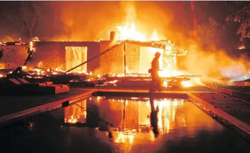  ?? — THE ASSOCIATED PRESS ?? A firefighte­r walks between a burning home and a swimming pool in Malibu. California wildfires have forced hundreds of thousands of people from their homes and destroyed at least 6,700 structures.