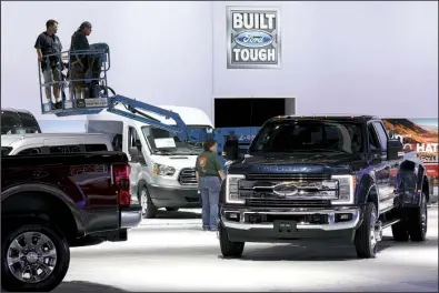  ?? Bloomberg News/PATRICK T. FALLON ?? Workers operate a lift near Ford Motor Co. pickups displayed at the company’s booth at the Los Angeles Auto Show in November. After seven straight years of sales gains, U.S. auto sales are expected to drop off in 2017, analysts said Wednesday.