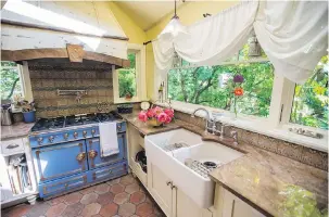  ??  ?? The blue enamel stove has copper knobs, while the hood above was fashioned by Waterglass Studios using parts from France. A long linen table runner was made into loops over the window and the floor tiles were hand-made in Maryland.