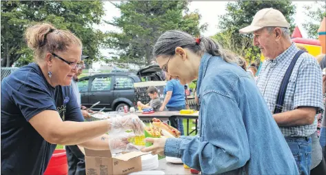  ?? KATHERINE HUNT/THE GUARDIAN ?? Union of Veterans Affairs Employees member Valerie Quinn, from left, serves up some hotdogs and corn to Demetra and Nabil Saroufim during a Labour Day picnic hosted at Joe Ghiz Memorial Park Monday. While the barbecue was a fun family event, it also saw union leaders advocate for a universal pharmacare plan.