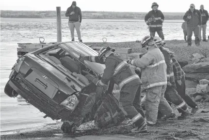  ?? DAVID JALA • CAPE BRETON POST ?? Firefighte­rs flip over a car after it was recovered from the water beside the Lingan Bay wharf on Sunday afternoon. The vehicle was apparently dumped in the water sometime after being stolen from a Sydney River residence on Christmas Eve.