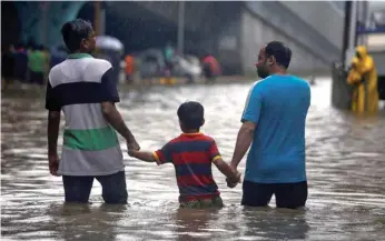  ?? — Reuters ?? People wade through a water-logged street after heavy rains in Mumbai on Saturday.