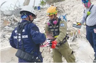  ?? (Screenshot) ?? AN ISRAELI search and rescue officer passes a stack of religious Jewish books to a South Florida counterpar­t after pulling them from the carnage of the collapsed building.