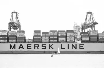  ?? — WP-Bloomberg photo ?? A sailing yacht passes in front of a container ship operated by the A.P. Moller-Maersk Group at the Port of Felixstowe in Felixstowe, England, on June 23.