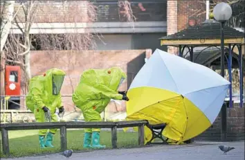  ?? Ben Stansall/AFP/Getty Images ?? Members of the emergency services in hazard suits afix a tent over the bench where a man and woman were found in critical condition Sunday at a shopping center in Salisbury, England.