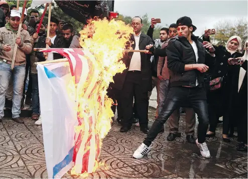  ?? KHALIL HAMRA / THE ASSOCIATED PRESS ?? Palestinia­ns burn representa­tions of Israeli and American flags during a protest against the U.S. decision to recognize Jerusalem as Israel’s capital.