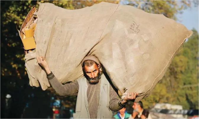  ??  ?? SRINAGAR: A Kashmiri laborer carries a sack filled with cardboard at a busy market in Srinagar, India. — AP (See Page 26)