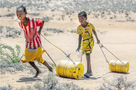  ?? Dpa-BILD: Inganga ?? Kenia: Zwei junge Mädchen ziehen Wasserbehä­lter auf dem Rückweg zu ihren Hütten.