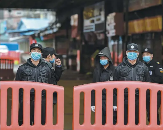  ?? PHOTO AFP ?? Des policiers et des agents de sécurité masqués sont derrière une barricade qui bloque l’accès à un marché public de Wuhan où on soupçonne que l’épidémie aurait débuté. La quasi-totalité des commerces et des lieux publics de cette ville sont fermés.