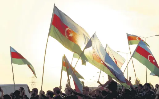  ??  ?? People wave flags at the funeral of an Azerbaijan­i soldier who was killed in Armenian shelling in the Tartar border district of Azerbaijan, Sept. 29, 2020.