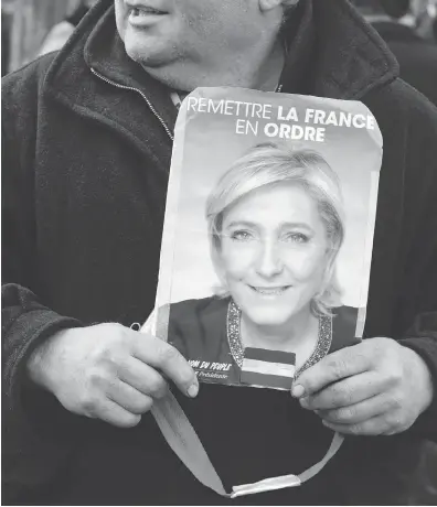  ?? JOEL SAGET / AFP / GETTY IMAGES ?? A supporter holds a Marine Le Pen electoral poster in Villepinte earlier this week.