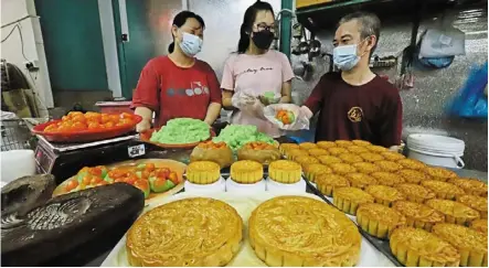  ??  ?? Labour of love: Loh making mooncakes with his wife and daughter at their shop in George Town.